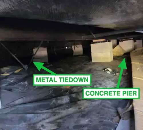 Crawl space of manufactured home showing metal tiedown and concrete piers